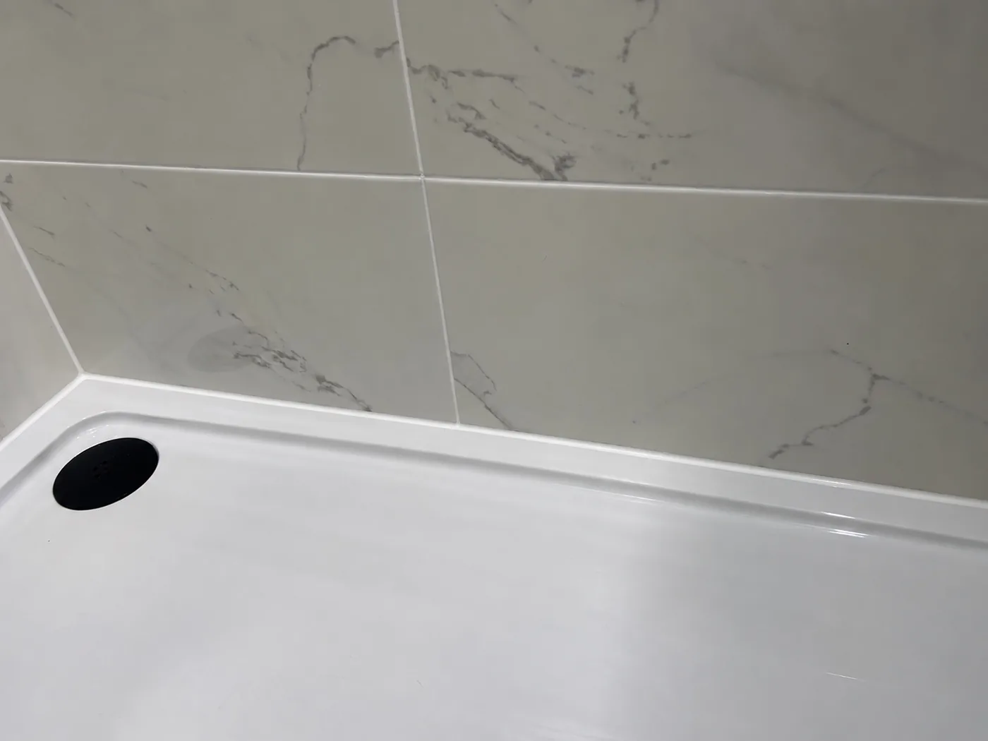 Fresh white silicone around a shower tray after resealing