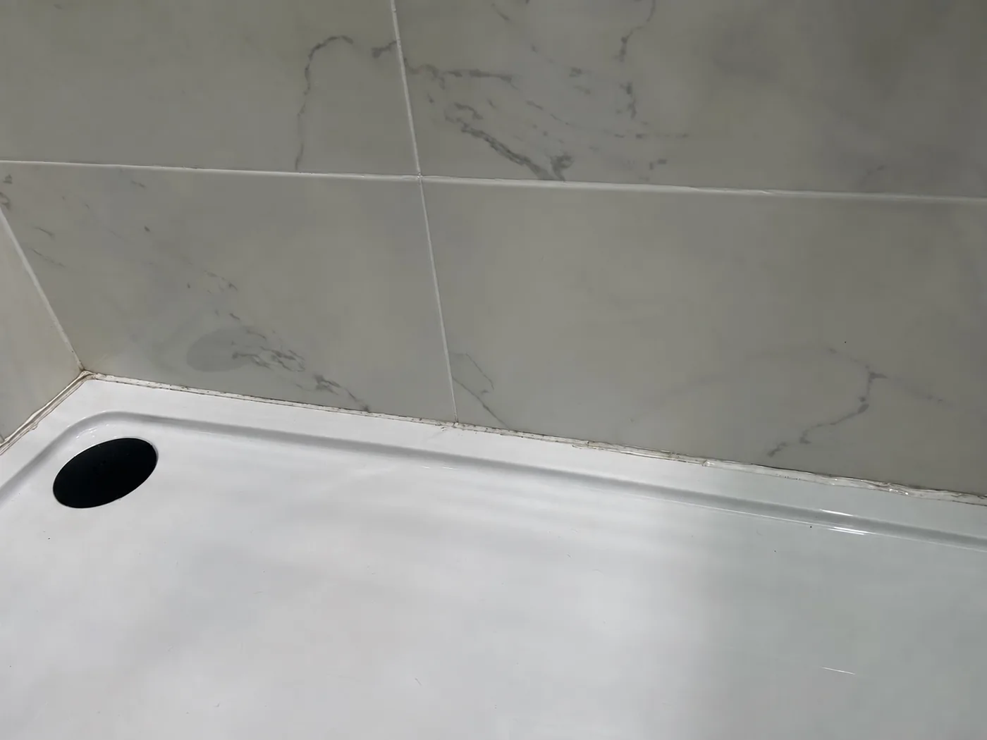 Old deteriorated silicone around a shower tray before replacement